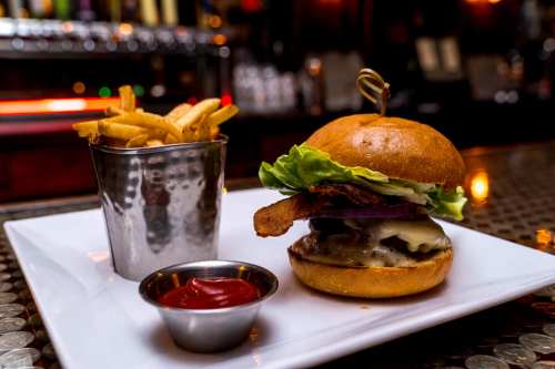 A juicy burger with lettuce, onion, and bacon, served with a side of fries and ketchup on a white plate.