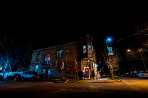 A dimly lit building at night, featuring colorful lights and flags, with parked cars nearby.
