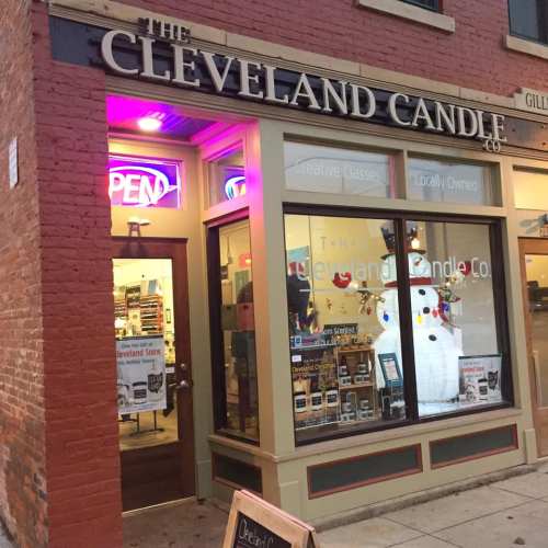 Exterior of The Cleveland Candle Co. shop, featuring an "OPEN" sign and a snowman decoration in the window.