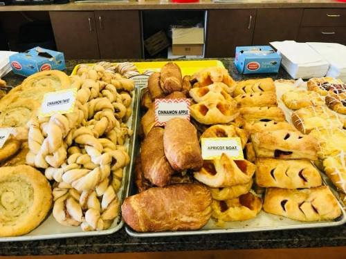 A variety of baked goods including cinnamon rolls, apple pastries, and apricot danishes displayed on trays.