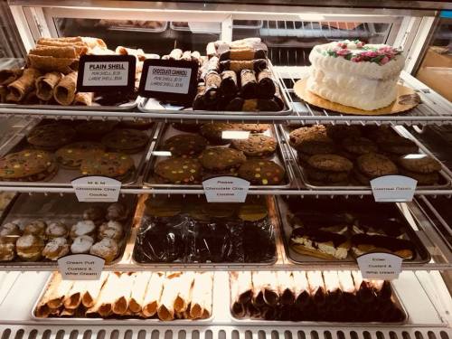 A display case filled with various baked goods, including cookies, pastries, and a decorated cake.