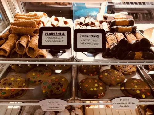 A display of pastries including cannoli, plain shells, and chocolate chip cookies with price tags.