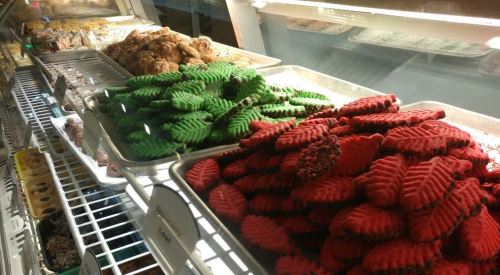 A display of colorful cookies in red and green leaf shapes, alongside other baked goods in a glass case.