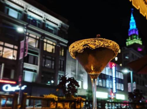 A close-up of a cocktail with a sugared rim, set against a vibrant city skyline at night.