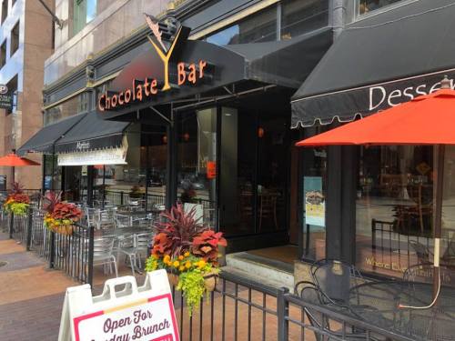 Exterior of Chocolate Bar with outdoor seating, colorful flowers, and a sign advertising brunch.