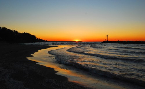 A serene beach at sunset, with gentle waves lapping at the shore and a warm orange sky reflecting on the water.