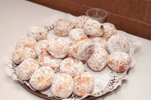 A platter of powdered sugar-coated doughnuts arranged on a lace doily.