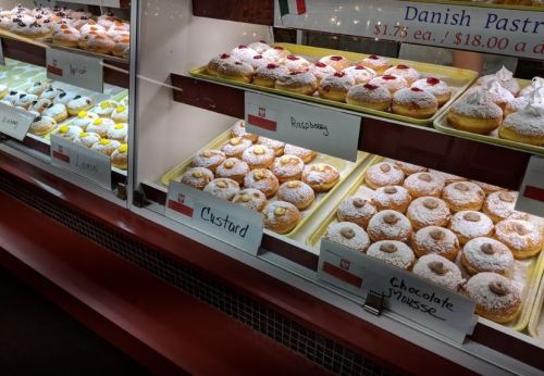 A display case filled with various pastries, including custard, raspberry, and chocolate mousse, dusted with powdered sugar.