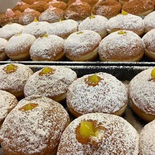 A close-up of freshly baked donuts dusted with powdered sugar, topped with yellow fruit filling.