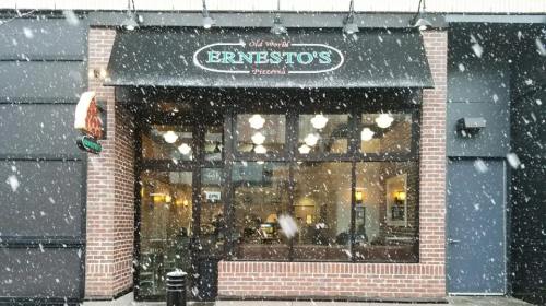 A cozy pizzeria named Ernesto's, with large windows, under a snowy sky. Warm lights glow inside.