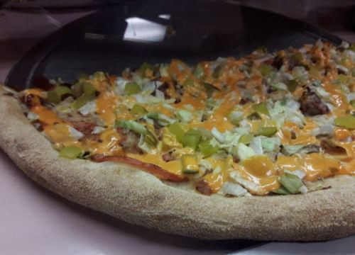 A close-up of a pizza topped with lettuce, green peppers, and a drizzle of orange sauce on a thick crust.