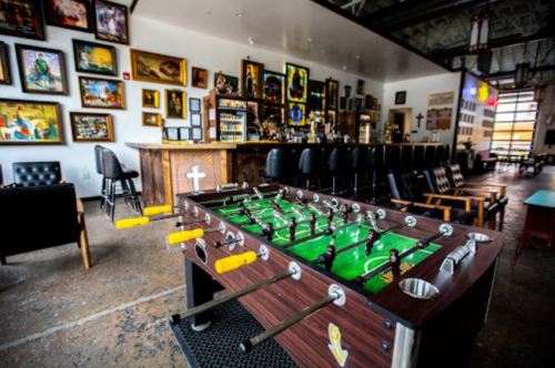 A foosball table in a bar with a rustic decor, featuring artwork on the walls and a wooden bar in the background.
