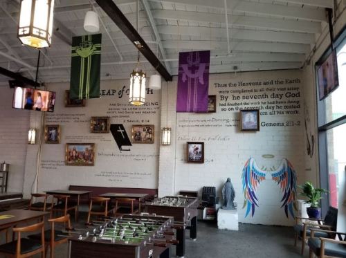 Interior of a cafe with religious banners, wall art, and a foosball table, featuring a bright, open atmosphere.