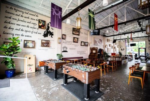 A spacious restaurant interior with wooden tables, foosball tables, and inspirational wall art.