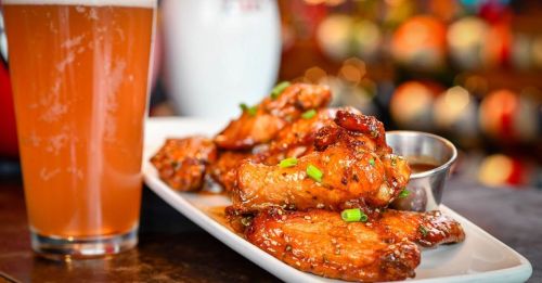 A plate of glazed chicken wings garnished with green onions, alongside a glass of amber beer.