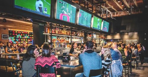 A lively bar scene with patrons enjoying drinks, multiple TVs showing sports, and a vibrant atmosphere.