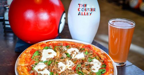 A delicious pizza topped with cheese and greens, alongside a drink, with a bowling pin and ball in the background.