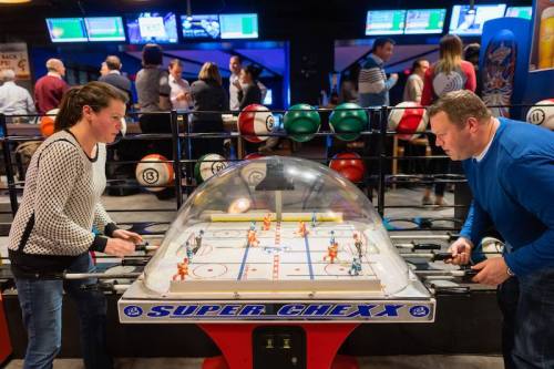 Two players compete at a Super Chexx bubble hockey game in a lively arcade setting.