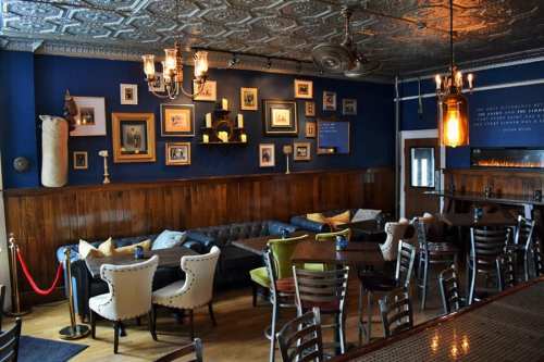 Cozy bar interior with dark blue walls, vintage decor, leather seating, and warm lighting.