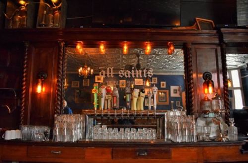 A vintage bar with a wooden counter, illuminated by warm lights, featuring beer taps and glassware.