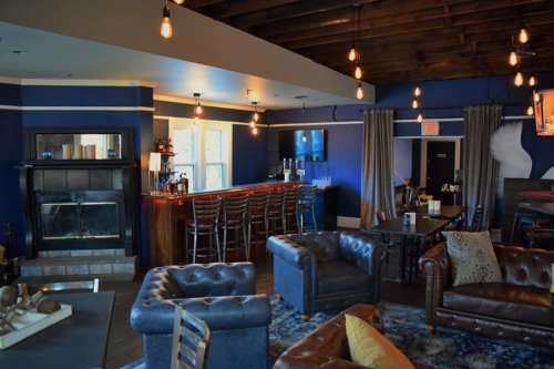 Cozy lounge with blue walls, leather sofas, a bar, and warm lighting, creating a welcoming atmosphere.