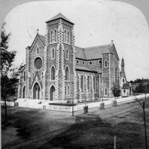 Historic black-and-white photo of a stone church with a large rose window and surrounding trees.