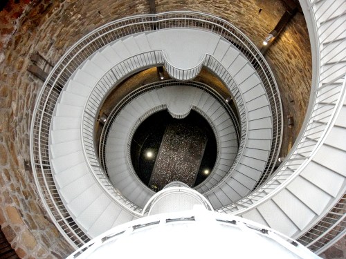 A spiral staircase viewed from above, showcasing a circular design and stone walls.