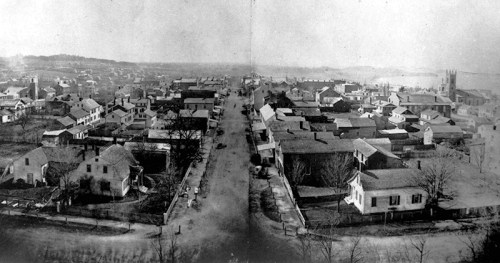 A historic black-and-white aerial view of a small town with houses, streets, and trees, showcasing early urban development.