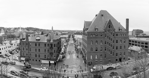 A panoramic black-and-white view of a city street lined with historic buildings and parked cars.