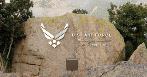 Sign for U.S. Air Force Cheyenne Mountain Air Force Station on a large rock, surrounded by trees and mountains.