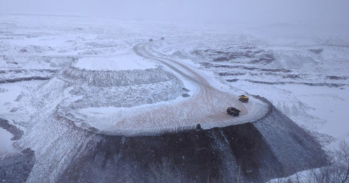A snowy landscape with a winding road and heavy machinery on a large, snow-covered mound.