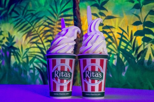 Two cups of soft-serve ice cream with white swirls, set against a colorful tropical background.
