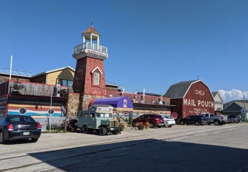 A colorful building with a lighthouse tower, vintage cars, and a sign for "Mail Pouch Tobacco Co." on a sunny day.