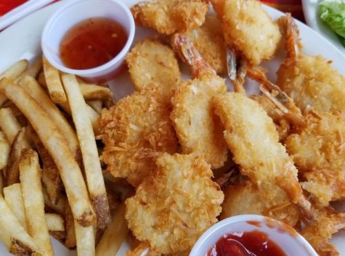A plate of crispy fried shrimp with French fries and two small cups of dipping sauce.