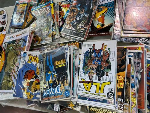 A pile of various comic books featuring colorful covers and different titles stacked together.