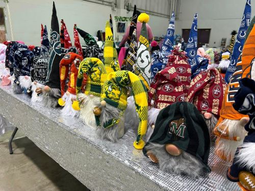 A row of colorful gnome figurines with various team-themed hats and fluffy beards displayed on a table.