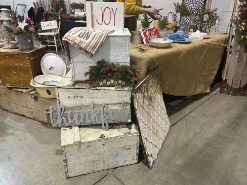 Decorative wooden crates stacked with signs reading "Joy" and "Thankful," surrounded by rustic decor at a market.