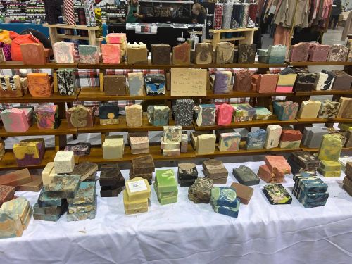 A display of various colorful handmade soaps arranged on wooden shelves at a market.