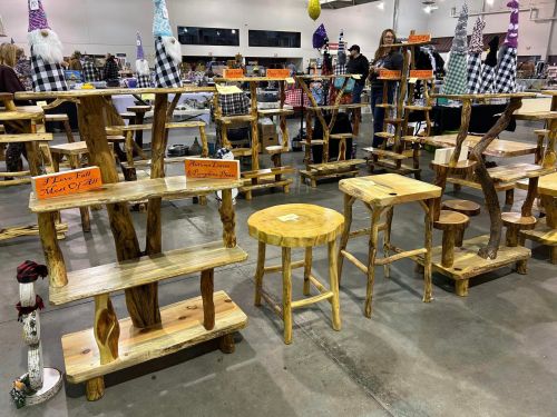 Wooden furniture displays at a craft fair, featuring various tables and stools with unique designs.