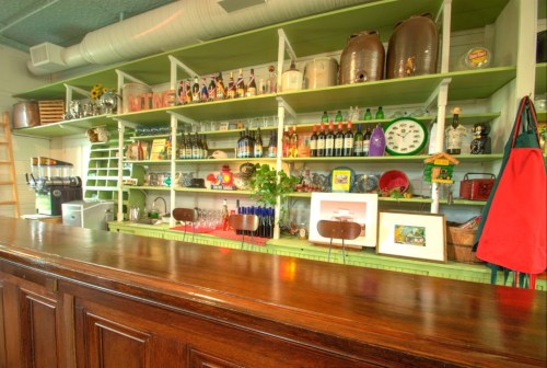 A colorful bar shelf filled with bottles, glassware, and decorative items, with a wooden counter in the foreground.