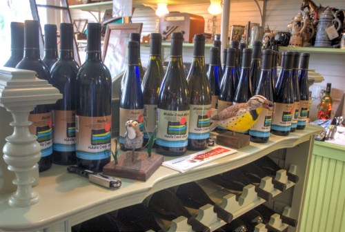 A display of wine bottles with colorful labels, alongside decorative bird figurines on a wooden shelf.