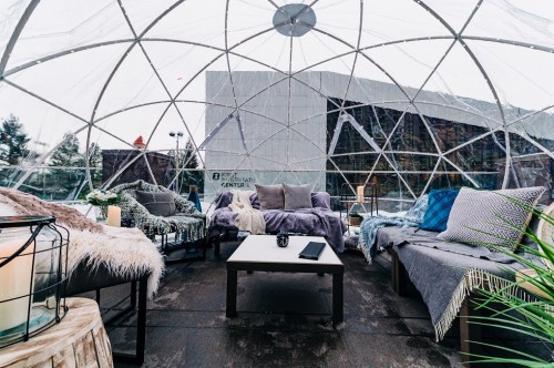 Cozy indoor seating area inside a transparent dome, featuring plush sofas, blankets, and a coffee table.