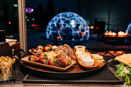 A beautifully arranged platter of chocolate-covered strawberries, cookies, and cheese, with a glowing igloo in the background.