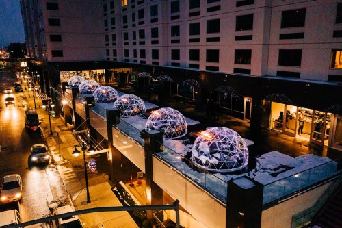 Aerial view of illuminated geodesic domes on a rooftop, surrounded by city buildings and evening traffic.