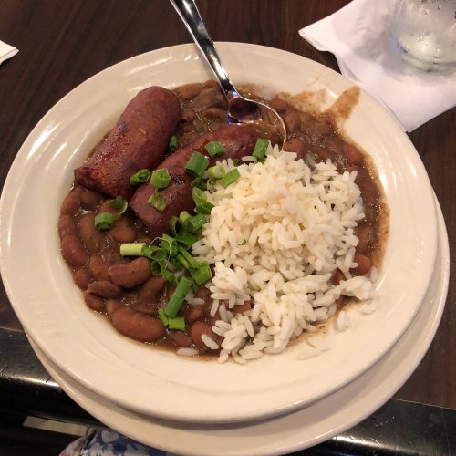 A plate of rice topped with green onions, served with pinto beans and a sausage link on the side.