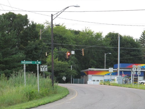 A road sign indicating Shelburne is 5 miles ahead, with a traffic light and a gas station in the background.