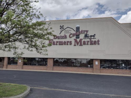 Exterior of Dutch Country Farmers Market with a sign and cloudy sky in the background.