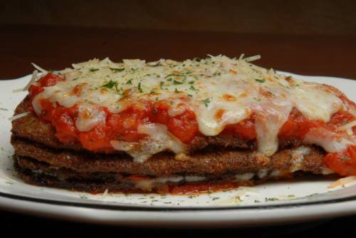 A layered dish featuring breaded and fried eggplant, marinara sauce, and melted cheese, garnished with herbs.