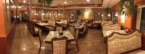 A cozy restaurant interior with booths, tables, and warm lighting, featuring plants and a tiled floor.