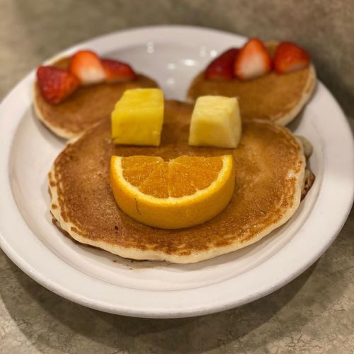 A plate of pancakes arranged to resemble a smiling face, topped with strawberries, orange, and pineapple.